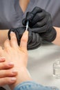 Painting female nails. Hands of manicurist in black gloves is applying transparent nail polish on female nails in a Royalty Free Stock Photo