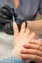 Painting female nails. Hands of manicurist in black gloves is applying transparent nail polish on female nails in a Royalty Free Stock Photo