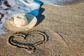 A painting of a heart on the beach with a staw hat and coming wave Royalty Free Stock Photo