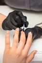 Painting nails of a woman. Hands of Manicurist in black gloves applying transparent nail polish on female Nails in a Royalty Free Stock Photo