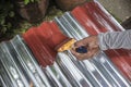 Painting the surface of a sheet of Galvanized Iron or GI corrugated metal with rust inhibiting red oxide primer Royalty Free Stock Photo