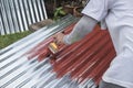 Painting the surface of a sheet of Galvanized Iron or GI corrugated metal with rust inhibiting red oxide primer Royalty Free Stock Photo