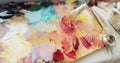 Paintress is mixing colourful oil paints on palette using brush, hand closeup.