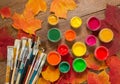 Paints, brushes, autumn leaves on wooden background. Royalty Free Stock Photo