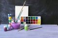 Paints, brushes, water on a wooden table against the background of a chalkboard