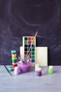 Paints, brushes, water on a wooden table against the background of a chalkboard