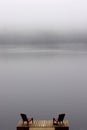 Pair of Adirondack chairs on wooden deck on lake in fog with copy space Royalty Free Stock Photo