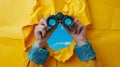 A pair of binoculars emerges through a torn yellow paper against a blue background.. AI generated Royalty Free Stock Photo