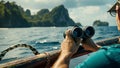 A pair of binoculars rests on the railing with a crew member peering through them towards the island in the distance