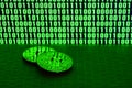 A pair of bitcoins lies on a cardboard surface on the background of a monitor depicting a binary code of bright green zeros and on