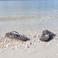Pair of black flipflops at the beach, a gentle tide going back and forth behind them