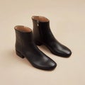 A pair of black leather ankle boots on a beige background Royalty Free Stock Photo