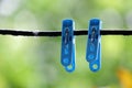 A pair of blue clothespins hanging on a black wire with raindrops in rainy day,blurred green nature background Royalty Free Stock Photo