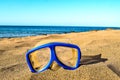 A pair of blue goggles sits on the sand next to the ocean Royalty Free Stock Photo