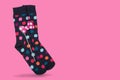 A pair of blue socks with multi-colored peas, on a pink background, as if standing on toes, with a decorative bow on a stick,