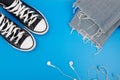 Pair of sneackers, wireless headphones and blue jeans are lying on a blue background. Top view. Flatlay. Copyspace center