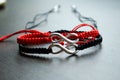 Pair bracelets in black and red with infinity. Handmade woven bracelets. Handmade decorations. Background with beads with hearts Royalty Free Stock Photo