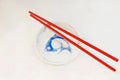 A pair of bright red melamine chopsticks and small porcelain serving dish with image of blue carp