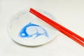 A pair of bright red melamine chopsticks on small porcelain serving dish with image of blue carp