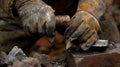 A pair of calloused hands adorns aged gloves skillfully operating a mallet and chisel to reveal a glimmer of dwindling