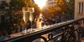 A pair of champagne glasses stand on the railing of a romantic balcony in the center of a European city, on sunset.