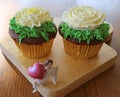 Pair of chocolate cupcakes with flower shaped whipped cream and a blurry mini angel with big heart figurine in foreground