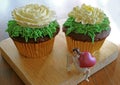 Pair of chocolate cupcakes topped with flower shaped whipped cream with a mini angel holding big heart on wooden tray