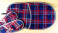 Pair of of colorful comfortable, cushioned, checkered disposable slippers and another very large are on the wooden floor. Top view