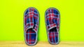 A pair of colorful comfortable, cushioned, checkered disposable slippers leaned against yellow wall. Close-up