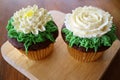 Pair of cupcakes decorated with flower shaped whipped cream served on wooden tray