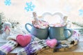 A pair of cups with a drink decorated with meringues and marshmallow snowmen, Christmas decor, hearts, a knitted scarf on the wind