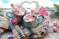 A pair of cups with a drink decorated with meringues and marshmallow snowmen, Christmas decor, hearts, a knitted scarf on the wind