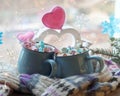 A pair of cups with a drink decorated with meringues and marshmallows, Christmas decor, hearts, knitted scarf on the windowsill