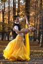 Pair of dancers dancing in the woods. Man with suit, woman in yellow long dress middle of the palace park in autumn. Dry fallen c Royalty Free Stock Photo