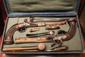 A pair of historic dueling pistols with accessories in an open case displayed in a museum.