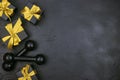 A pair of dumbbells and gifts with gold ribbons on a black background. Holiday fitness sale or black friday concept