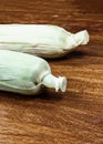 Pair of ears of corn whole vegetables with green leaves on wooden tinted background