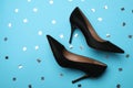 Pair of elegant black high heel shoes and confetti on light blue background, flat lay. Space for text Royalty Free Stock Photo