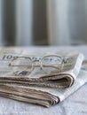 A pair of eyeglasses lies on a stack of folded newspaper on a minimalist background. Generative AI Royalty Free Stock Photo