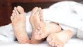 Pair of feet playing footsie under the covers at home in bed