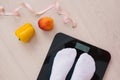 Pair of female feet in white socks standing on a scale with vegetables and fruits and a measuring tape or tape near them Royalty Free Stock Photo