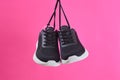 Pair female sports sneakers for run and fitness hanging by shoelaces on pink background. Fashion stylish sport shoes.