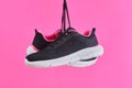 Pair female sports sneakers for run and fitness hanging by shoelaces on pink background. Fashion stylish sport shoes.