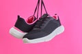 Pair female sports sneakers for run and fitness hanging by shoelaces on pink background. Fashion stylish sport shoes