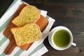 Pair of Garlic Butter Toasts on Breadboard with a Cup of Hot Green Tea on Wooden Table