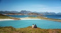 A pair of girls sit on the cliff with view of beautiful landscape, traveling to Norway on the Lofoten Islands