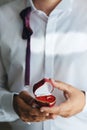 Pair of gold wedding rings in red heart-shaped box in hands of groom on wedding day vertical shot Royalty Free Stock Photo