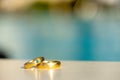 A pair of Golden Wedding Rings with Turquoise Diamond in Front of a Hotel Pool