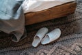 The pair of gray home slippers near the wooden bed on the