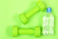 Pair of green fitness dumbbells and bottle of water.